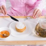 Vista parziale della donna in pigiama che ha frittelle con marmellata per la colazione a letto a casa