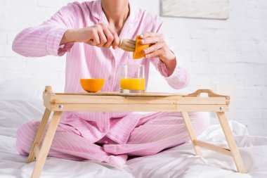 partial view of woman with wooden pestle making fresh orange juice in bed in morning at home clipart