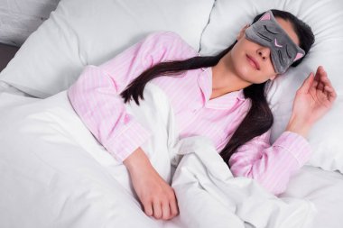 Pembe pijama ve uyku maskesi evde yatakta uyuyan kadın portresi