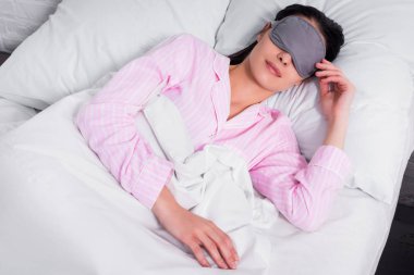 Pembe pijama ve uyku maskesi evde yatakta uyuyan kadın portresi