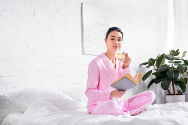pijama ile fincan sıcak çay ve kitap yatağa sabah evde oturan kadın