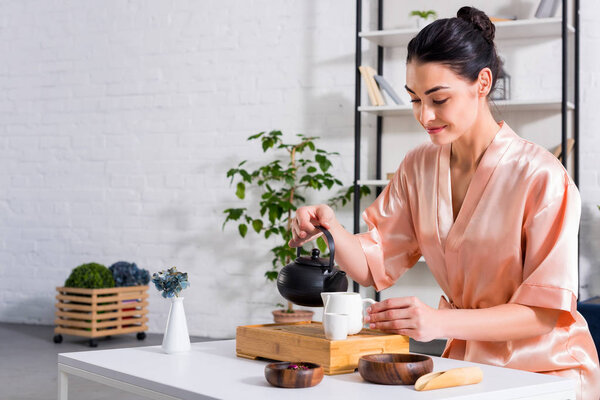 attractive woman in silk bathrobe making tea while having tea ceremony in morning at home