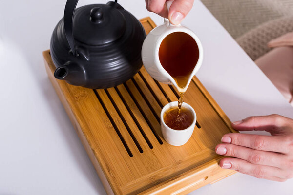 partial view of woman pouring tea into cup while having tea ceremony at home