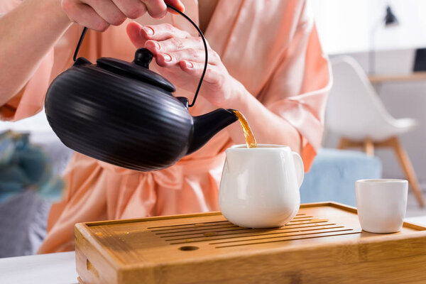 partial view of woman pouring tea into jug while having tea ceremony at home