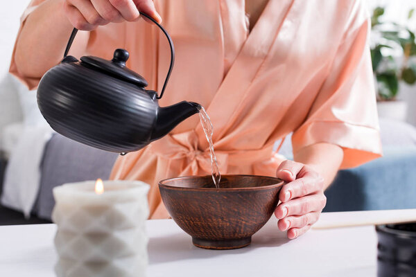 cropped shot of woman making tea while having tea ceremony in morning at home