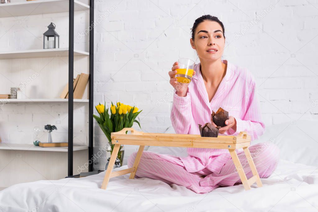 woman in pajamas with glass of orange juice and chocolate muffins on bed in morning at home