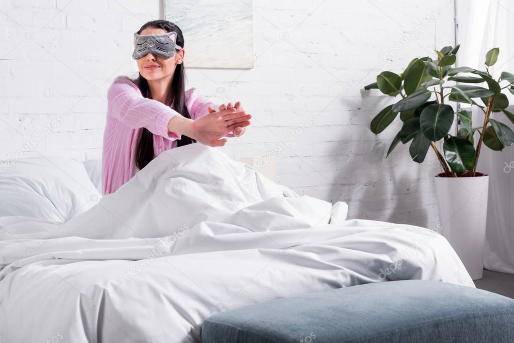 woman in pink pajamas and sleeping mask stretching in bed in morning