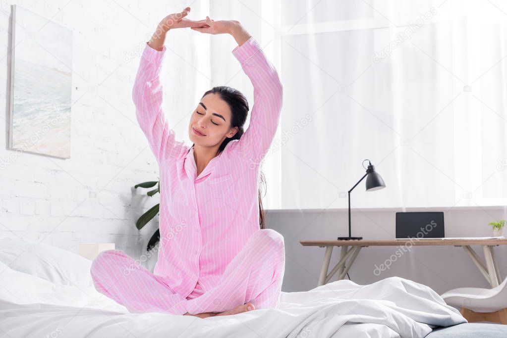 woman in pajamas stretching on bed in morning at home