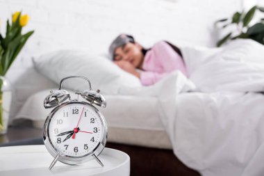 Saat ve Pembe pijama ve uyku maskesi evde yatakta uyuyan kadın seçici odak