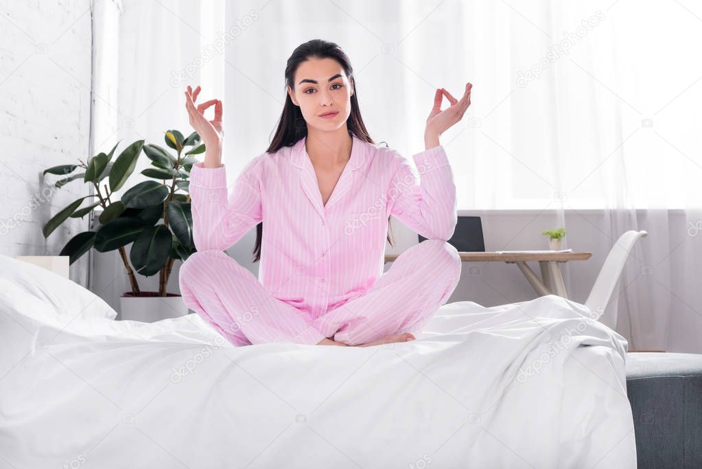 woman in pink pajamas sitting in lotus pose on bed in morning at home