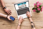 Schnappschuss eines Mannes mit Smartphone mit Facebook-Logo in der Hand und einer Frau am Tisch mit Laptop mit Amazon-Website und Kalanchoe-Blume