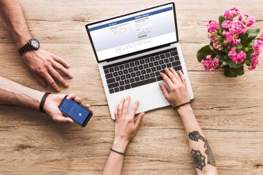 Kırpılan atış bir adam ile el ve masa laptop facebook Web sitesi ve aranjmani çiçekli kadın facebook logosu ile smartphone