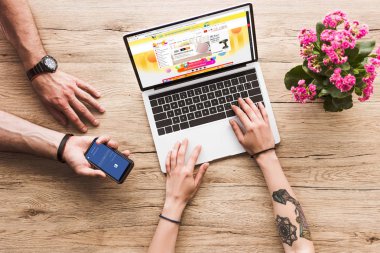 Kırpılan atış bir adam ile el ve aliexpress Web sitesi ve aranjmani çiçek ile dizüstü bilgisayar ile masa üstü kadına facebook logosu ile smartphone