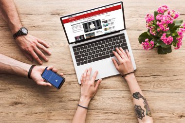 Kırpılan atış bir adam ile el ve bbc Web sitesi ve aranjmani çiçek ile dizüstü bilgisayar ile masa üstü kadına facebook logosu ile smartphone