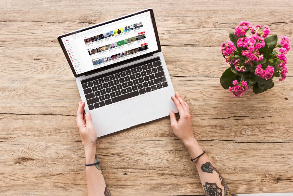 Partial view of woman at tabletop with laptop with youtube website and kalanhoe plant in flowerpot