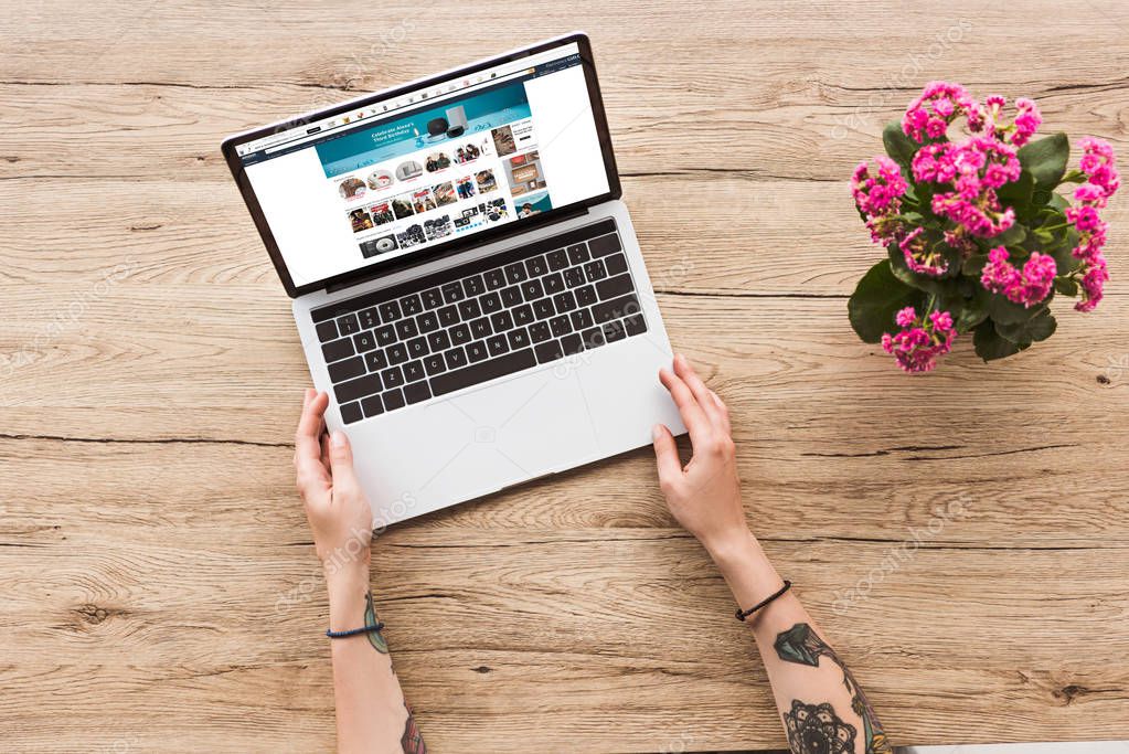 Partial view of woman at tabletop with laptop with amazon website and kalanhoe plant in flowerpot