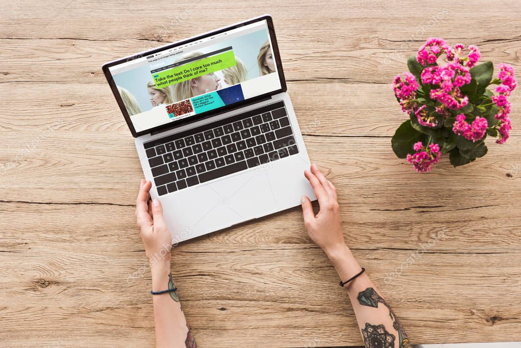 Partial view of woman at tabletop with laptop with bbc website and kalanhoe plant in flowerpot