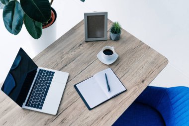 Tablo boş ekran, boş ders kitabı, fotoğraf çerçevesi, Saksı bitki ve kahve fincanı ile dizüstü yükseltilmiş görünümü 