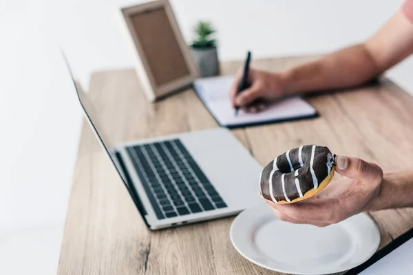 Uomo Possesso Ciambella Scrittura Libro Testo Tavola Con Computer Portatile — Foto Stock