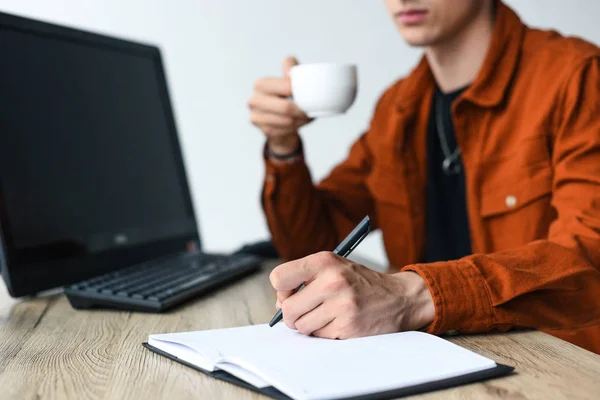 Partial View Man Drinking Coffee Writing Textbook Table Computer Computer — Stock Photo, Image