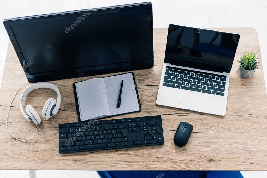 elevated view of table with laptop, computer, empty textbook, pen and headphones 