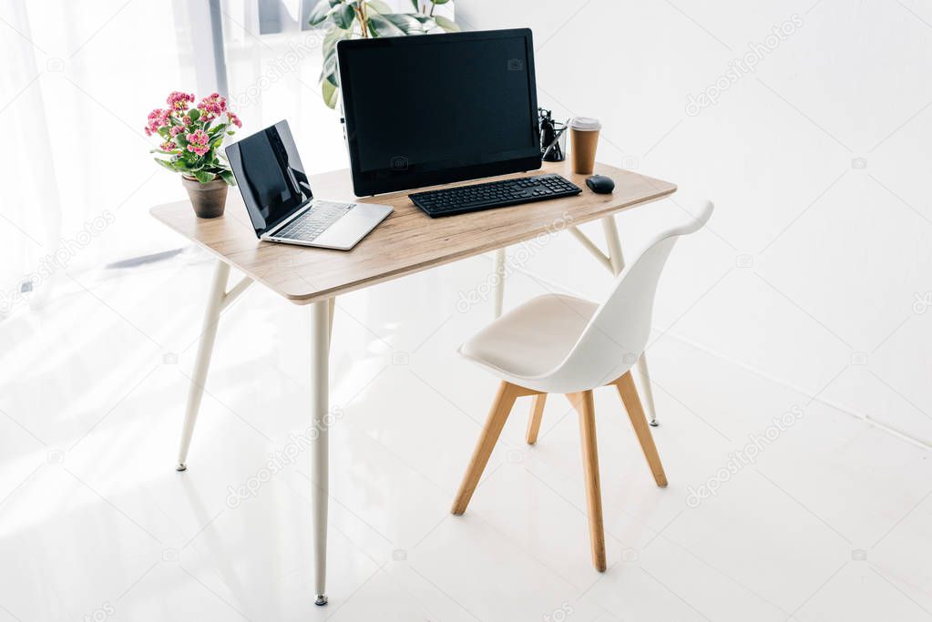 interior of workplace with chair, flowers, coffee, stationery, laptop and computer on wooden table 