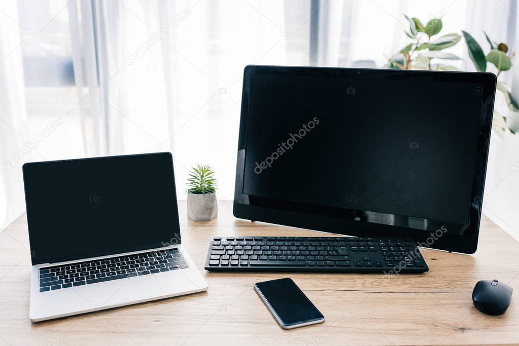 closeup shot of laptop with blank screen, computer, smartphone and potted plants on wooden table 