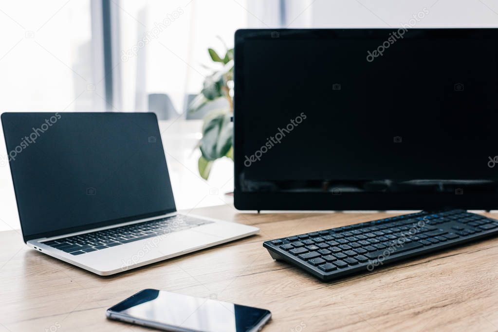 closeup view of smartphone with blank screen, laptop and computer at wooden table 