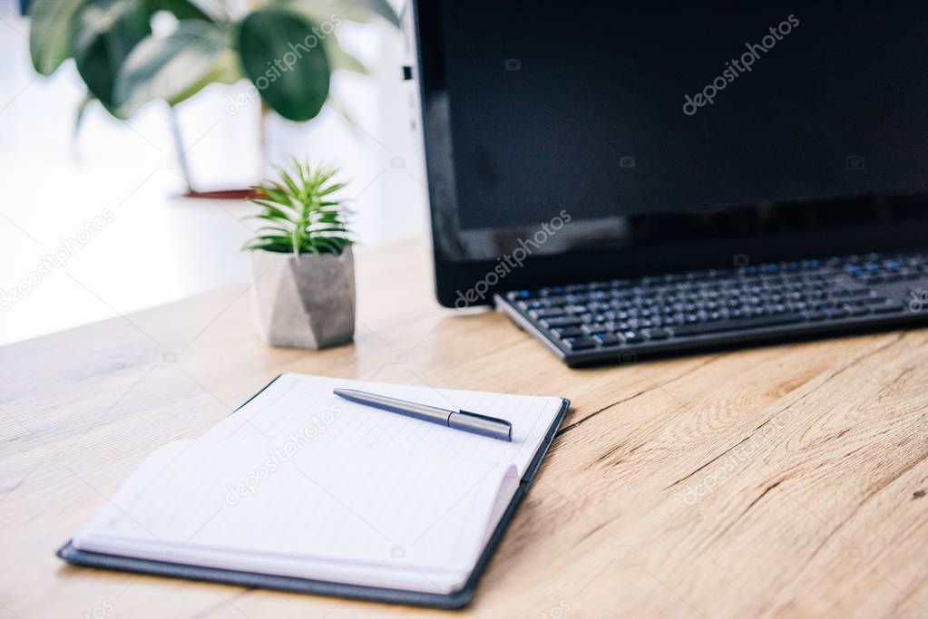 closeup image of empty textbook, pen, potted plant, computer and computer keyboard at table