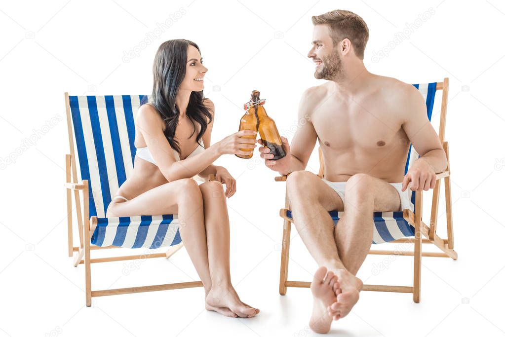 boyfriend and girlfriend clinking with bottles of beer while relaxing on beach chairs, isolated on white  