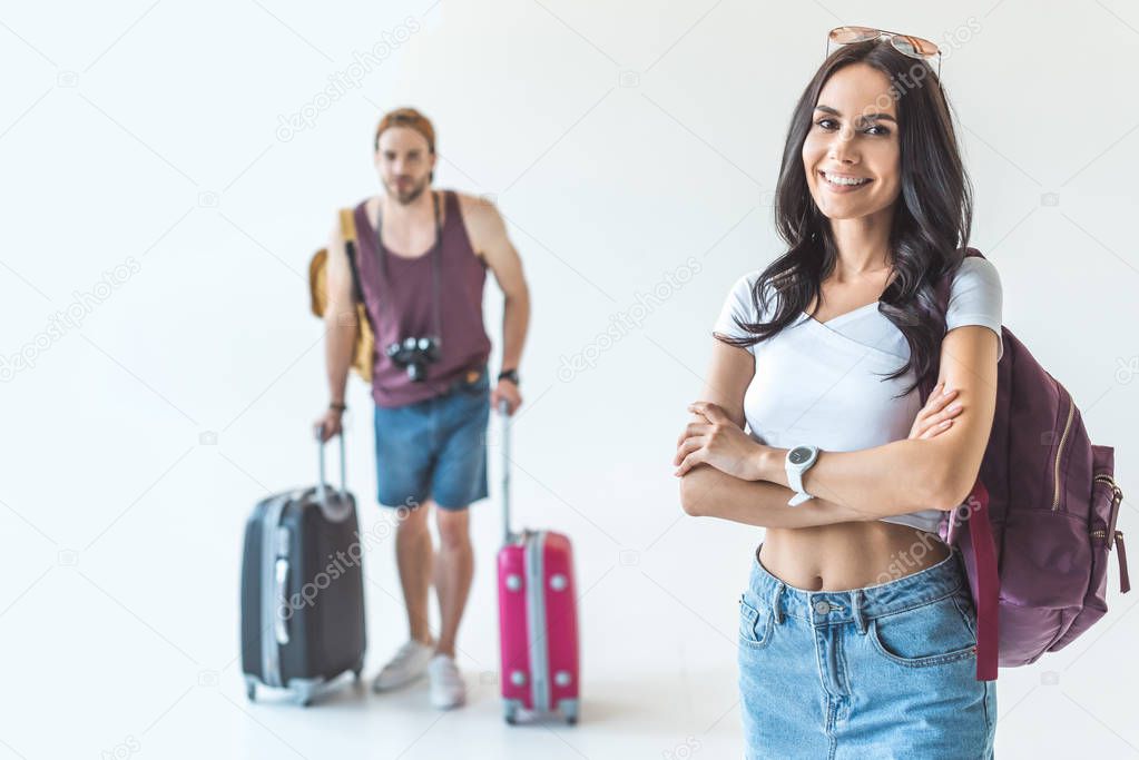 selective focus of woman with crossed arms and boyfriend with travel bags, isolated on white