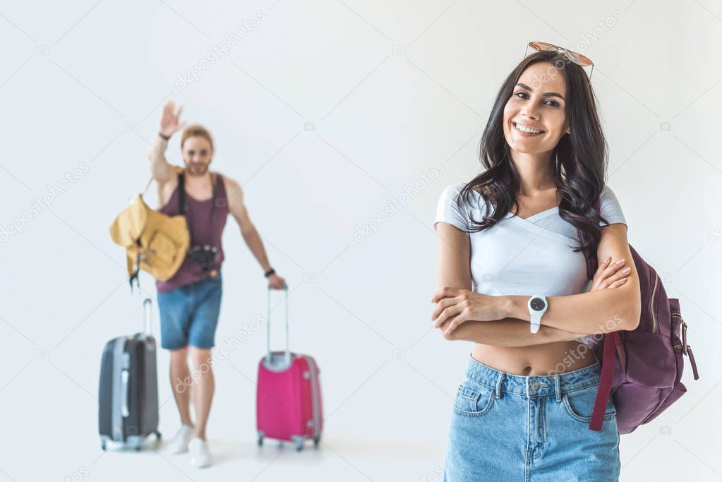 smiling girl with crossed arms and boyfriend with travel bags, isolated on white