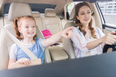portrait of smiling woman driving car and daughter pointing away on passengers seat clipart