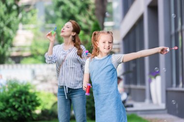 Anne ve gülümseyen kız parkta sabun köpüğü üfleme