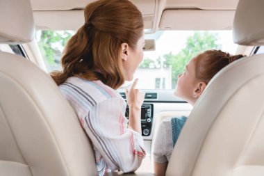 back view of mother showing something to daughter on passengers seat in car clipart