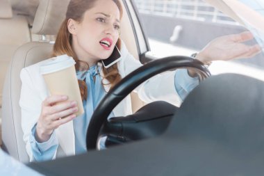 businesswoman with cup of coffee in hand talking on smartphone while driving car clipart