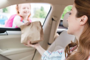 seçici odak bir arabada kağıt paket gıda ile kızı veren anne