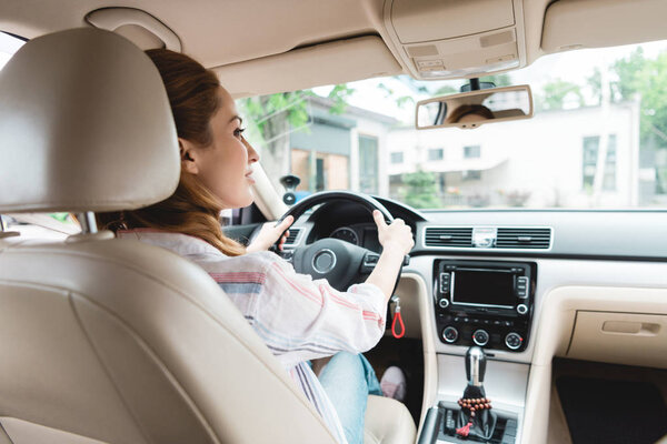 вид сзади женщины, отводящей взгляд за рулем автомобиля
