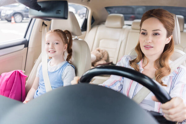 портрет женщины за рулем автомобиля с улыбкой дочери на пассажирском сиденье
