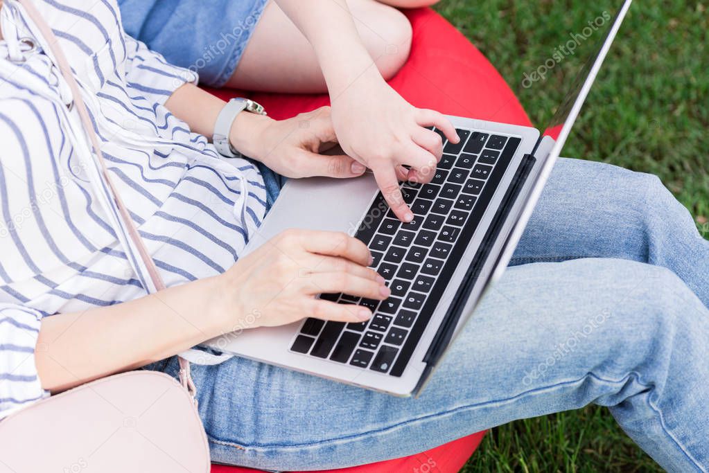 partial view of mother and daughter using laptop while resting on bag chair together