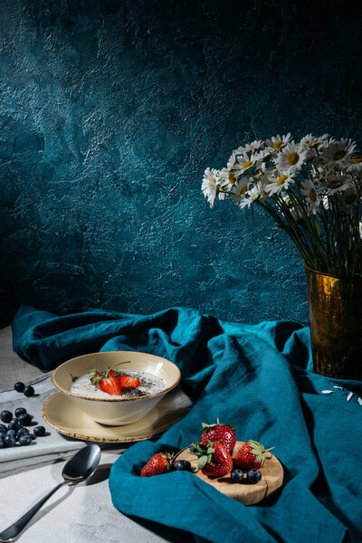 Bowl with chia seeds and ripe summer berries on table with tablecloth and flowers