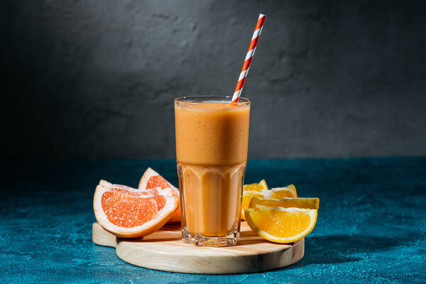 Glass of juice with orange and grapefruit pieces on wooden board