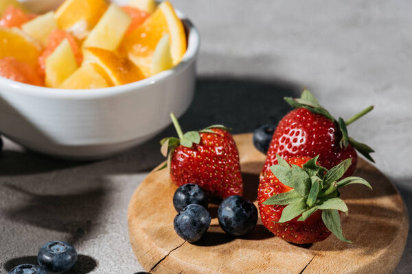 Strawberries and blueberries on wooden board by bowl with citrus fruits