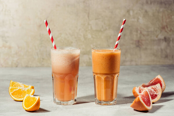 Fresh juice in glasses with orange and grapefruit pieces on table