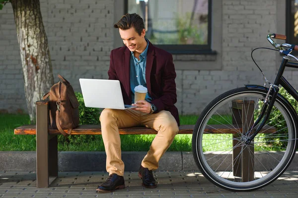 Uśmiechający Się Freelancer Młodych Trzymając Kubek Papierowy Pomocą Laptopa Siedząc — Zdjęcie stockowe