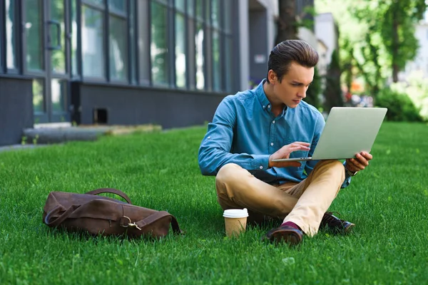 专注的年轻人使用膝上型电脑和坐在草地上 — 图库照片