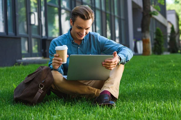 Uśmiechający Się Freelancer Młodych Trzymając Kubek Papierowy Pomocą Laptopa Siedząc — Zdjęcie stockowe