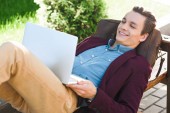 boldog fiatal szabadúszó padon fekve és használ laptop