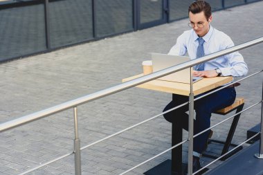 yakışıklı genç iş adamı dışarıda otururken dizüstü kullanarak gözlük yüksek açılı görünüş