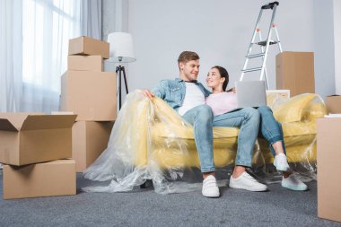 beautiful young couple using laptop while sitting on couch at new home clipart